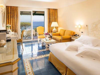 Světý hotelový pokoj s manželskou postelí, posezením a výhledem na moře přes velká okna