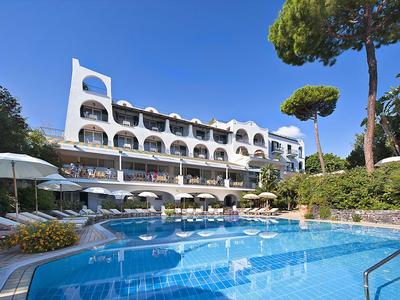 Modernes Hotel mit weißen Fassaden, Balkonzimmern und Außenpool unter blauem Himmel.
