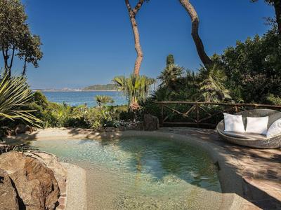 Kleiner Pool mit Sandstrand und Pflanzen, im Hintergrund Meer und blauer Himmel.