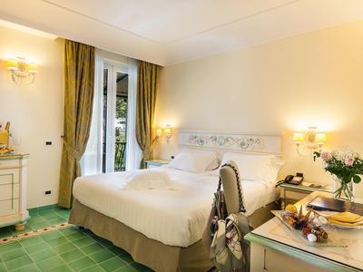 Pohodlný hotelový pokoj s velkou postelí, zelenými závěsy a dlaždicovou podlahou.