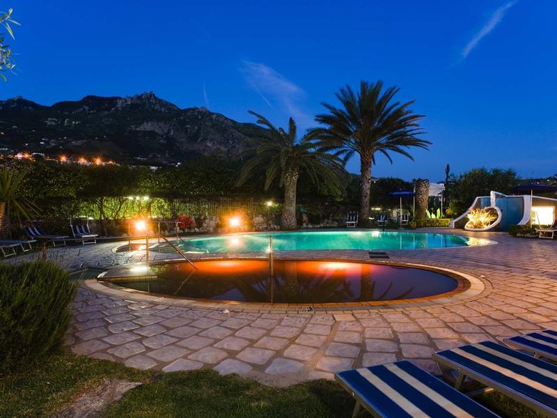 Verlichte zwembadgebied met palmbomen en ligstoelen 's nachts