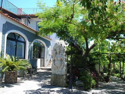 Außenbereich eines Hotels mit geschwungenen großen Fenstern, Steinfigur und grüner Vegetation