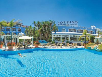 Gran piscina de hotel con cómodas tumbonas y palmeras bajo un cielo azul claro.