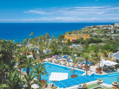 Resort mit Pool, Palmen und Meerblick unter blauem Himmel.