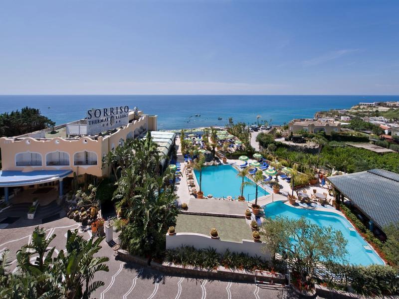 Hotel mit Poolanlage, Palmen und Blick auf das blaue Meer unter klarem Himmel.