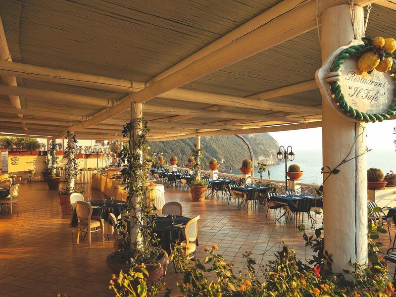 Großes offenes Restaurant mit Holzmöbeln und Blick auf Berge und Meer bei Sonnenuntergang.