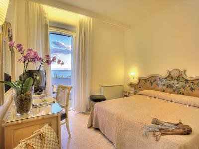 Chambre d'hôtel confortable avec lit double, fleurs, bureau et balcon avec vue sur la mer.