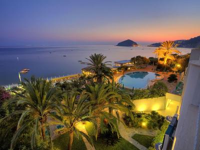 Vue d'un hôtel éclairé avec piscine et palmiers au bord de la mer au coucher du soleil.