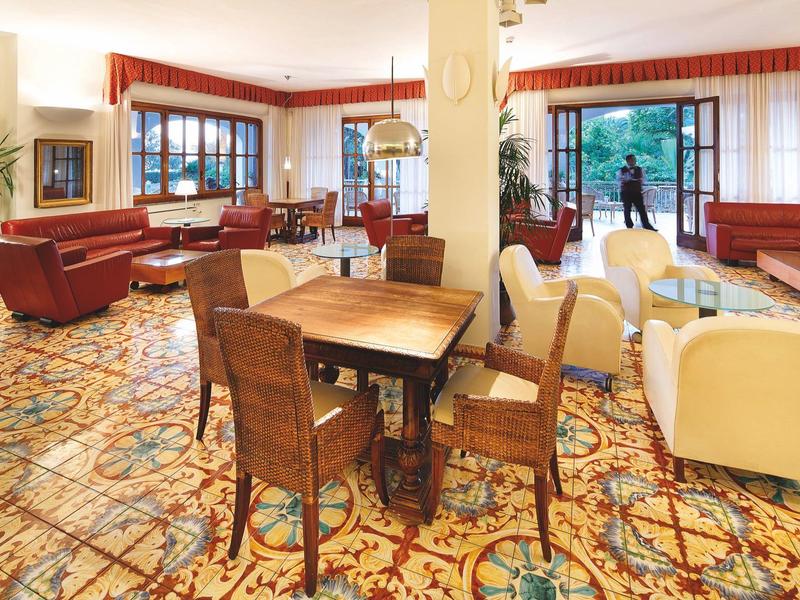 Jasna przestrzeń salonu hotelowego z kolorowym wzorzystym dywanem i różnorodnymi meblami.