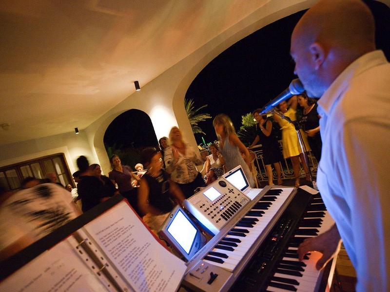 Muzyk gra na keyboardzie podczas wieczornej imprezy z tańczącymi gośćmi w otwartej przestrzeni.