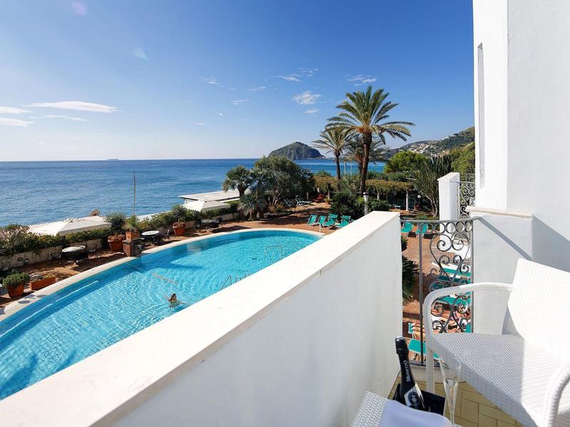 Widok z balkonu na basen, palmy i morze pod czystym niebem.