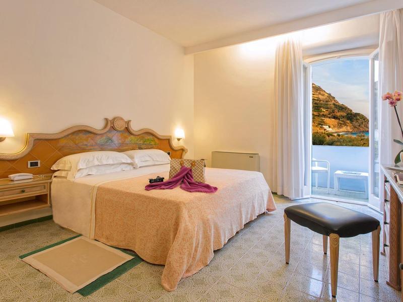 Jasno urządzony pokój hotelowy z podwójnym łóżkiem i widokiem na morze przez okno.