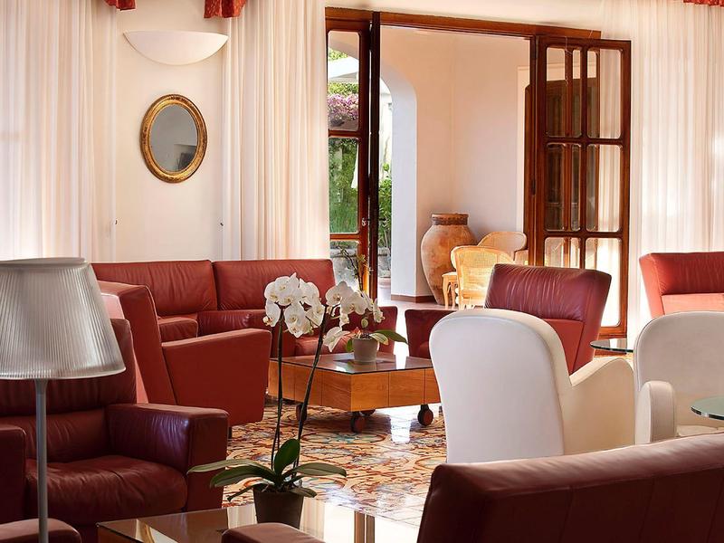 Elegancki salon z czerwonymi i białymi fotelami oraz otwartymi drzwiami na balkon.