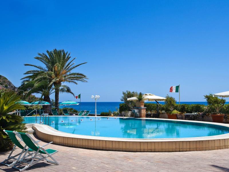 Okrągły basen z leżakami i palmami, widok na morze i niebieskie niebo.