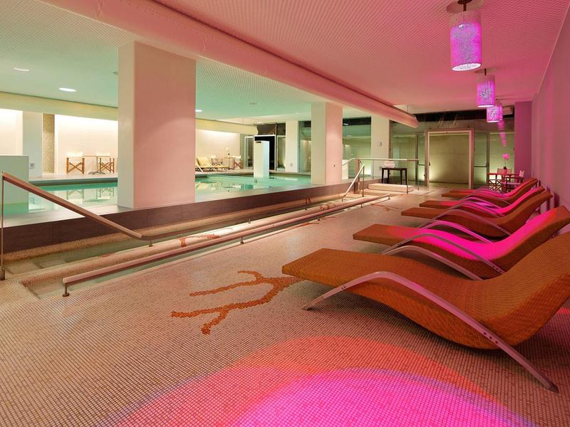 Nowoczesna strefa spa z leżakami i delikatnym oświetleniem obok krytego basenu.