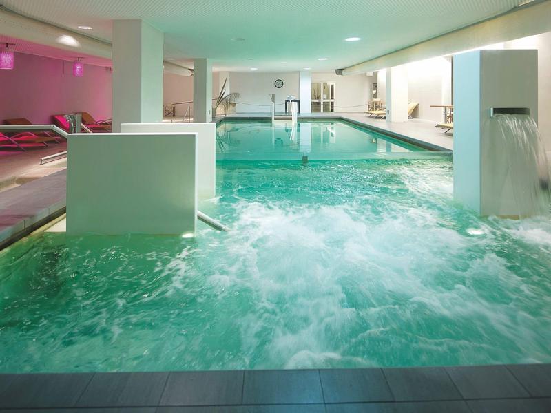 Basen kryty z jacuzzi i relaksującymi leżakami w nowoczesnej strefie wellness.