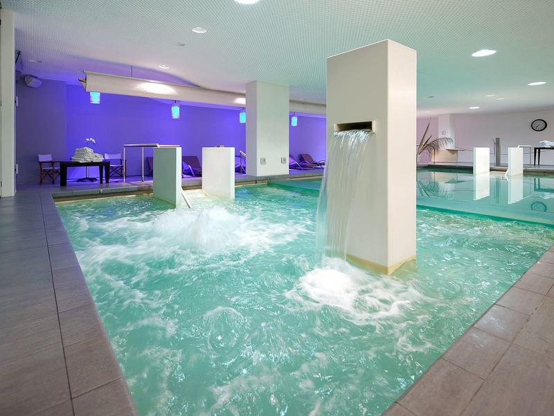 Nowoczesny basen kryty z fontannami wodnymi i relaksującym oświetleniem w strefie spa.