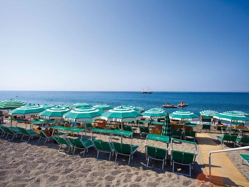 Plaża z rzędami zielonych leżaków i parasoli pod niebieskim niebem.