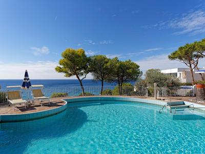 Kruhový bazén s výhledem na moře a lehátky pod modrou oblohou.