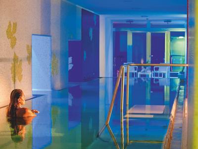 Žena relaxuje v atmosféricky osvětleném vnitřním bazénu s moderní architekturou.