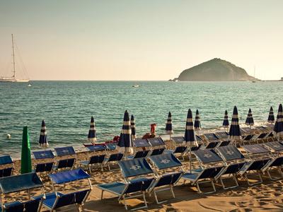 Sdraio vuote con ombrelloni sulla spiaggia davanti al mare e all'isola al tramonto.