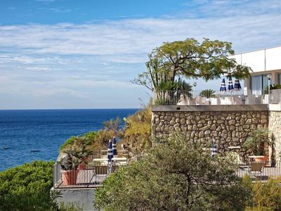 Pohled na terasu s stromy a posezením u moře pod jasnou oblohou.