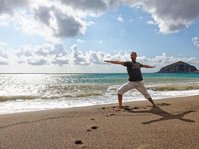 Osoba cvičí jógu na pláži za oblačného počasí a klidného moře.