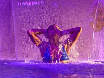 Osoba užívající si vodopád v osvětleném bazénu v noci