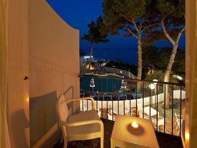 Balcone con sedie e tavolo di notte con vista sulla baia illuminata e alberi.