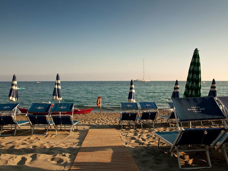 Prázdná lehátka a zavřené slunečníky na písečné pláži s výhledem na klidné moře.