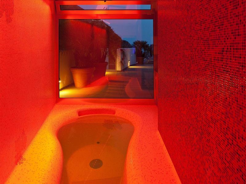 Červená koupelna s vanou před velkým oknem s výhledem na venkovní prostor za soumraku