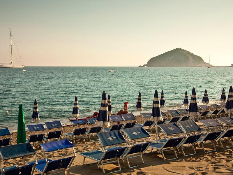 Mnoho prázdných lehátek s uzavřenými slunečníky na pláži při západu slunce.