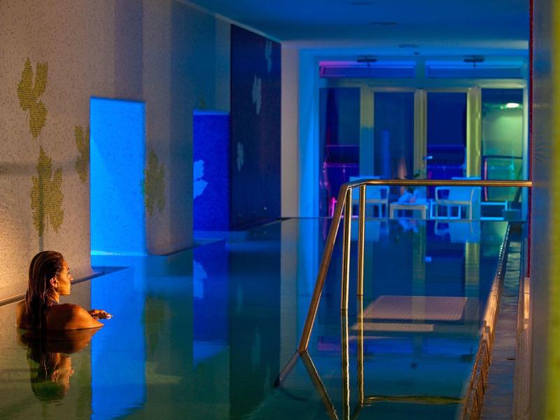 Žena odpočívající v vyhřívaném krytém bazénu moderního hotelu s modrým osvětlením.