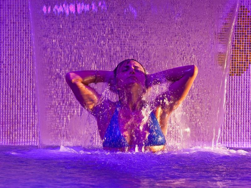 Osoba užívající si vodopád v osvětleném bazénu v noci