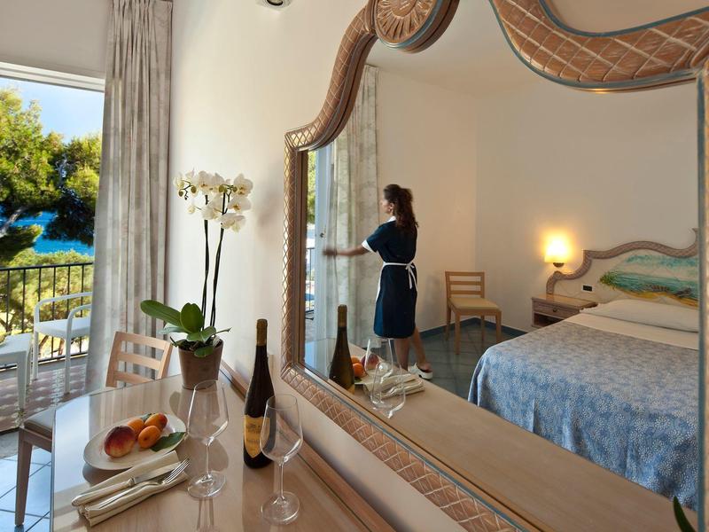 Ložnice s velkým zrcadlem, postelí, prostřeným stolem a výhledem na terasu a bazén.