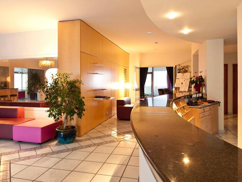 Světlá hotelová lobby s recepcí, posezením a rostlinami