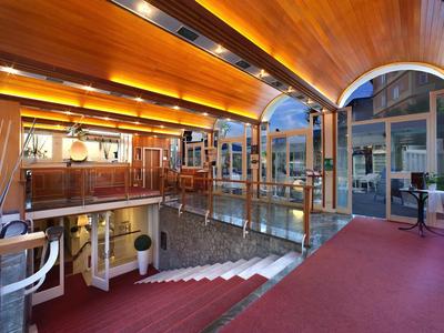 Elegancki hol hotelowy z czerwonym dywanem, szklanymi balustradami i ciepłym drewnianym wystrojem pod sklepionym sufitem.