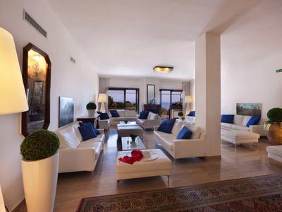 Jasny salon z białymi sofami, ozdobnymi poduszkami i dużymi oknami wpuszczającymi światło dzienne.