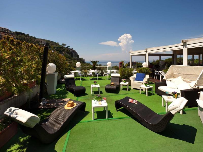 Nowoczesny taras z leżakami, stolikami i zieloną sztuczną trawą pod niebieskim niebem.