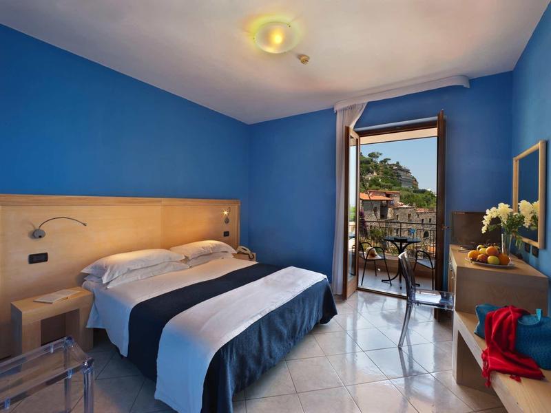 Pokój hotelowy z niebieskimi ścianami, podwójnym łóżkiem i balkonem z widokiem na palmy.