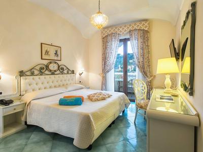 Camera d'hotel luminosa con letto matrimoniale, comodini, illuminazione e balcone con vista.