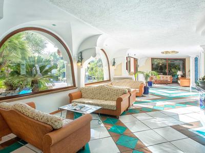 Jasna strefa wypoczynkowa hotelu z brązowymi meblami i dużymi oknami łukowymi.