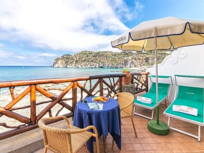 Balcone con vista mare, tavolo con due sedie e ombrellone accanto a due lettini.