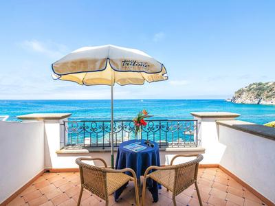 Widok z tarasu z stołem, krzesłami i parasolem na niebieskie morze i skały.