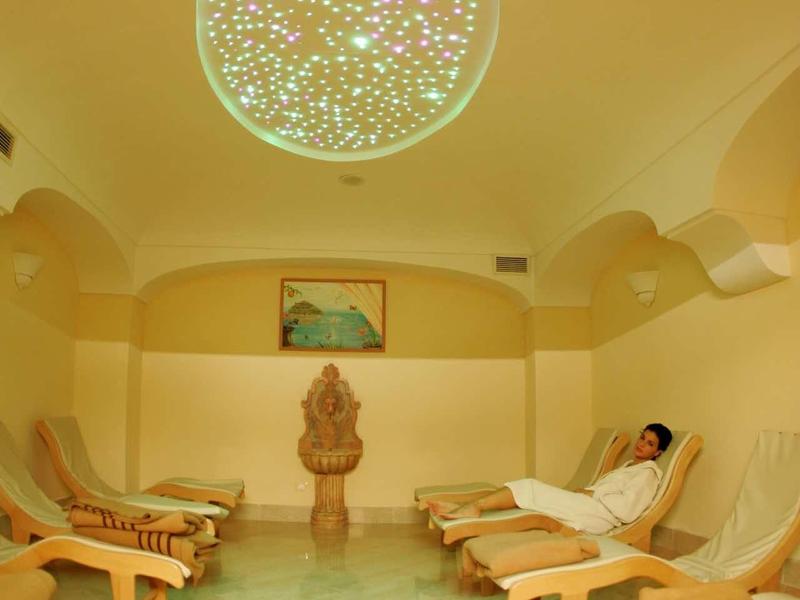 Sala relax con lettini, luce calda e lampada decorativa sul soffitto in ambiente luminoso.