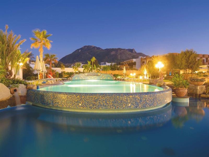 Piscina illuminata con bacino d'acqua rotondo e ambiente tropicale al crepuscolo.