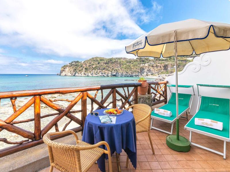 Balcone con vista mare, tavolo con due sedie e ombrellone accanto a due lettini.