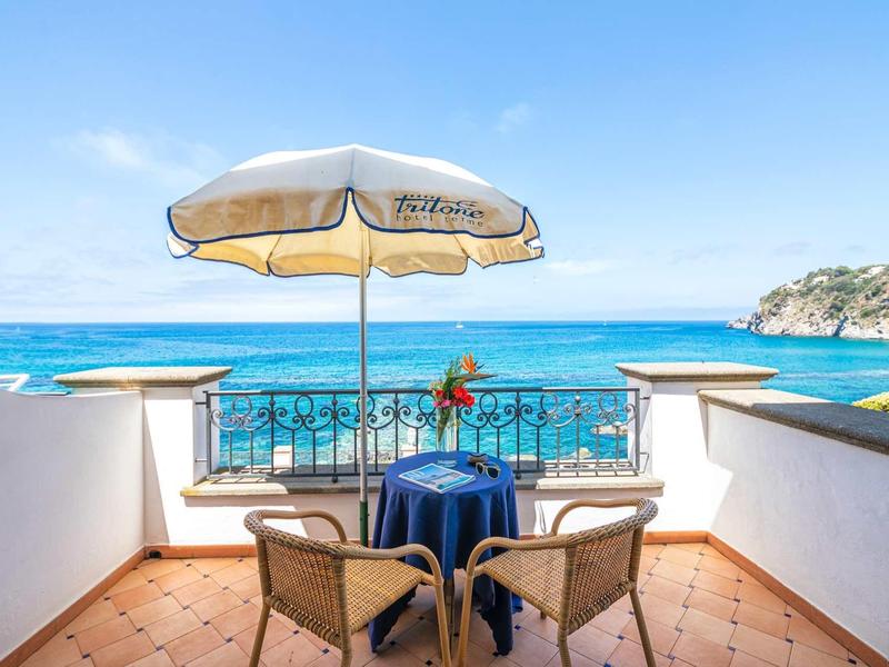 Vista sul mare da una terrazza con tavolo, due sedie e ombrellone.
