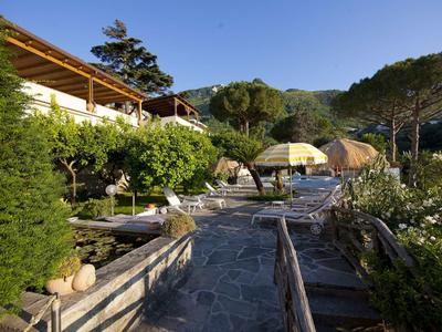 Gepflasterter Weg mit Holzgeländer, Liegestühlen, Sonnenschirm und grüner Berglandschaft bei klarem Himmel.