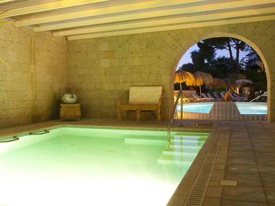 Innenpool mit hellem Wasser, Steinwänden, Holzbalkendecke und Ausblick auf Außenpool und Garten.